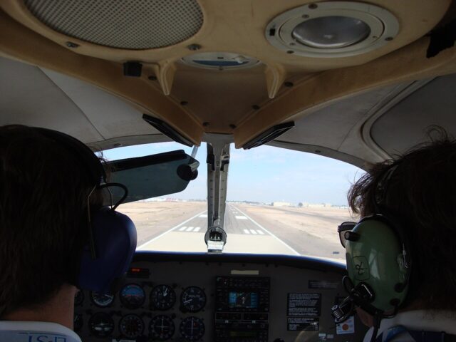 Two pilots in a small-aircraft cockpit approaching a runway at Phoenix Goodyear Airport.