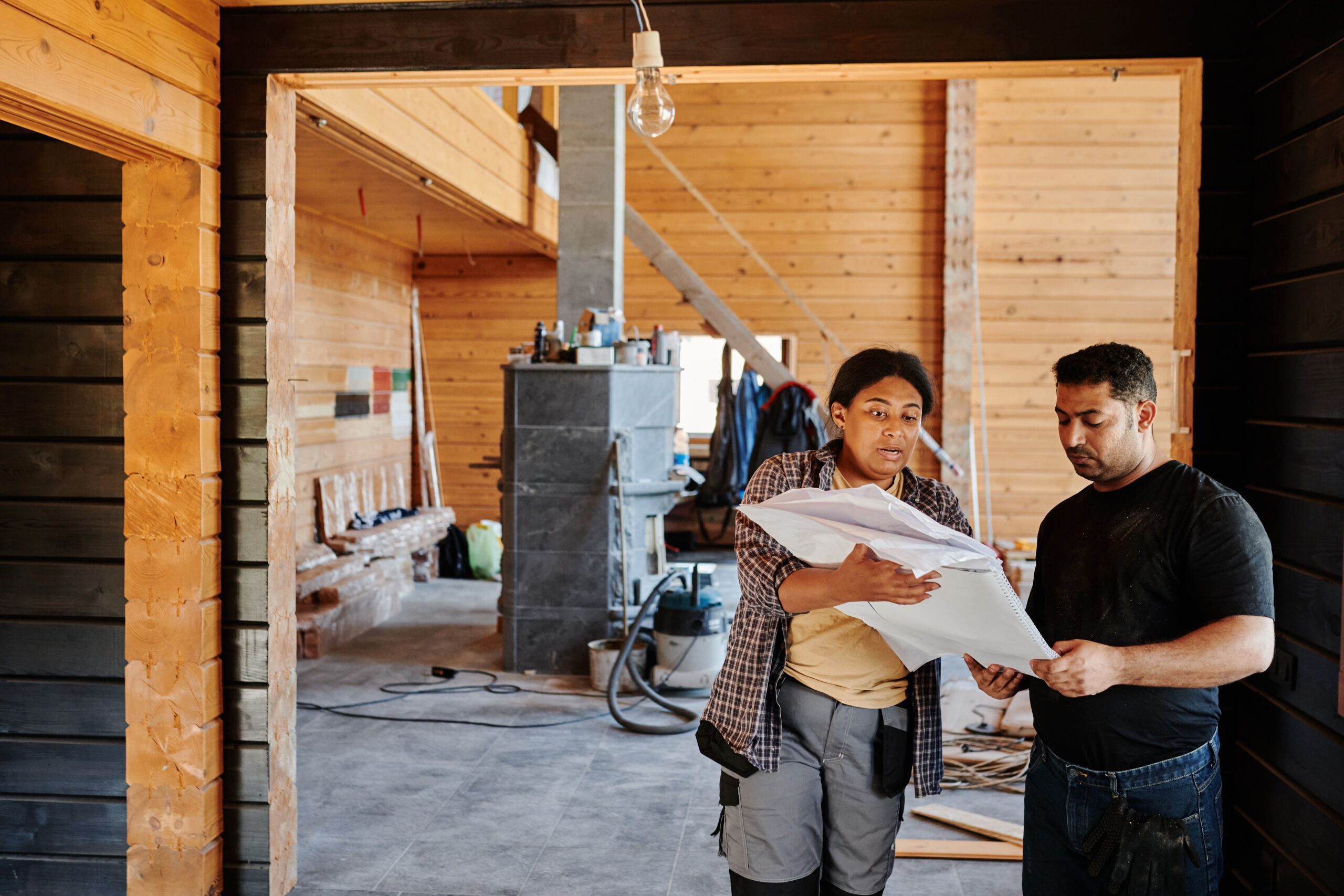 Two construction professionals reviewing renovation blueprints inside a partially finished building.